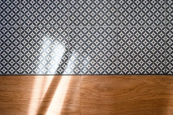 Sol carrelé de carreaux géométriques gris et blancs au-dessus d'un parquet.