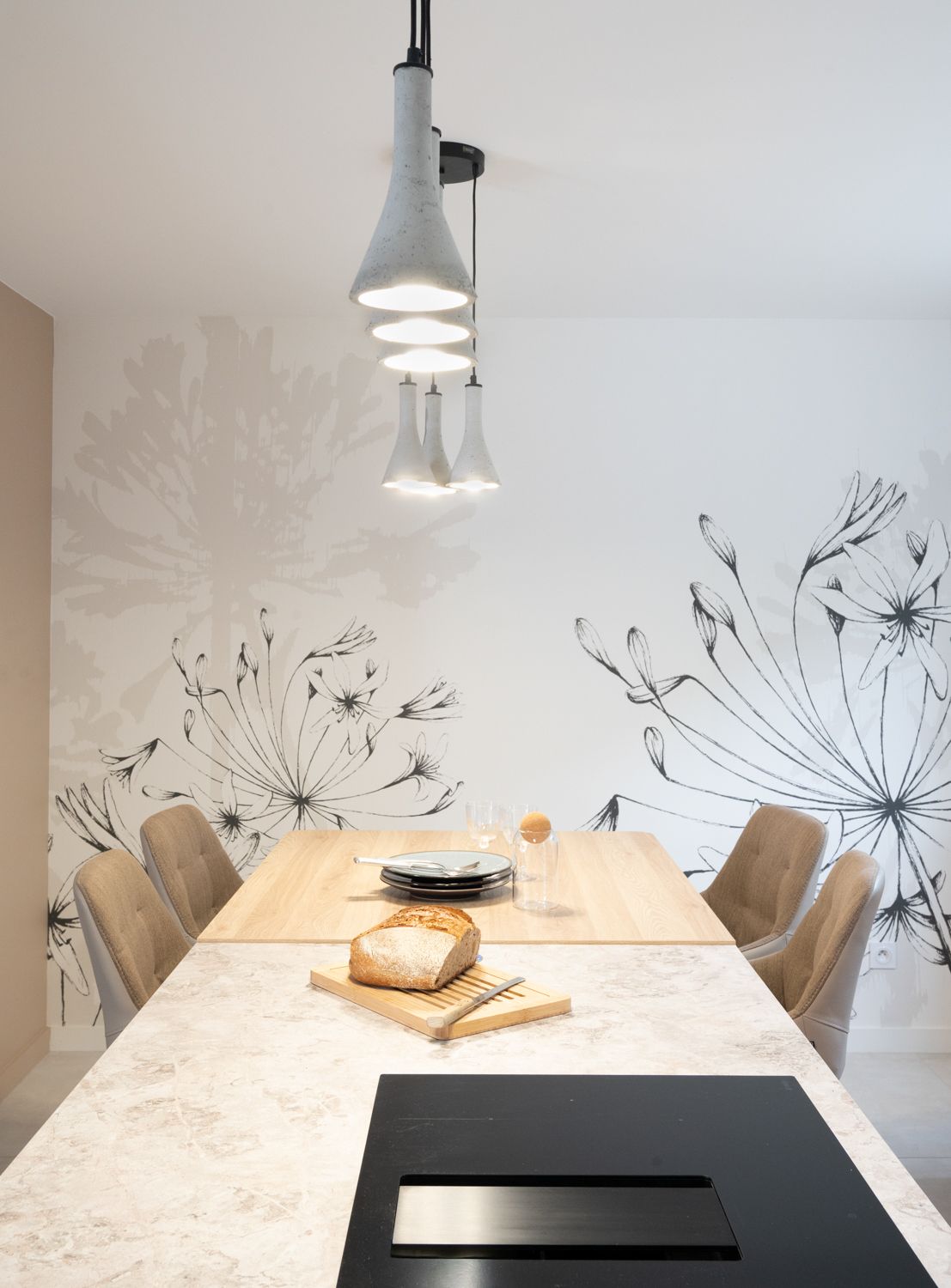 Coin repas avec une table en bois, des suspensions lumineuses et une fresque murale de pissenlits.