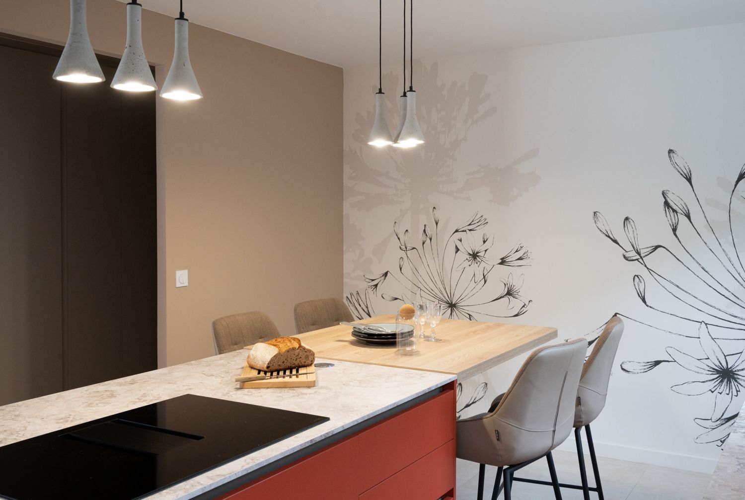 Cuisine moderne avec îlot central, table à manger, suspensions lumineuses et fresque murale florale décorative.
