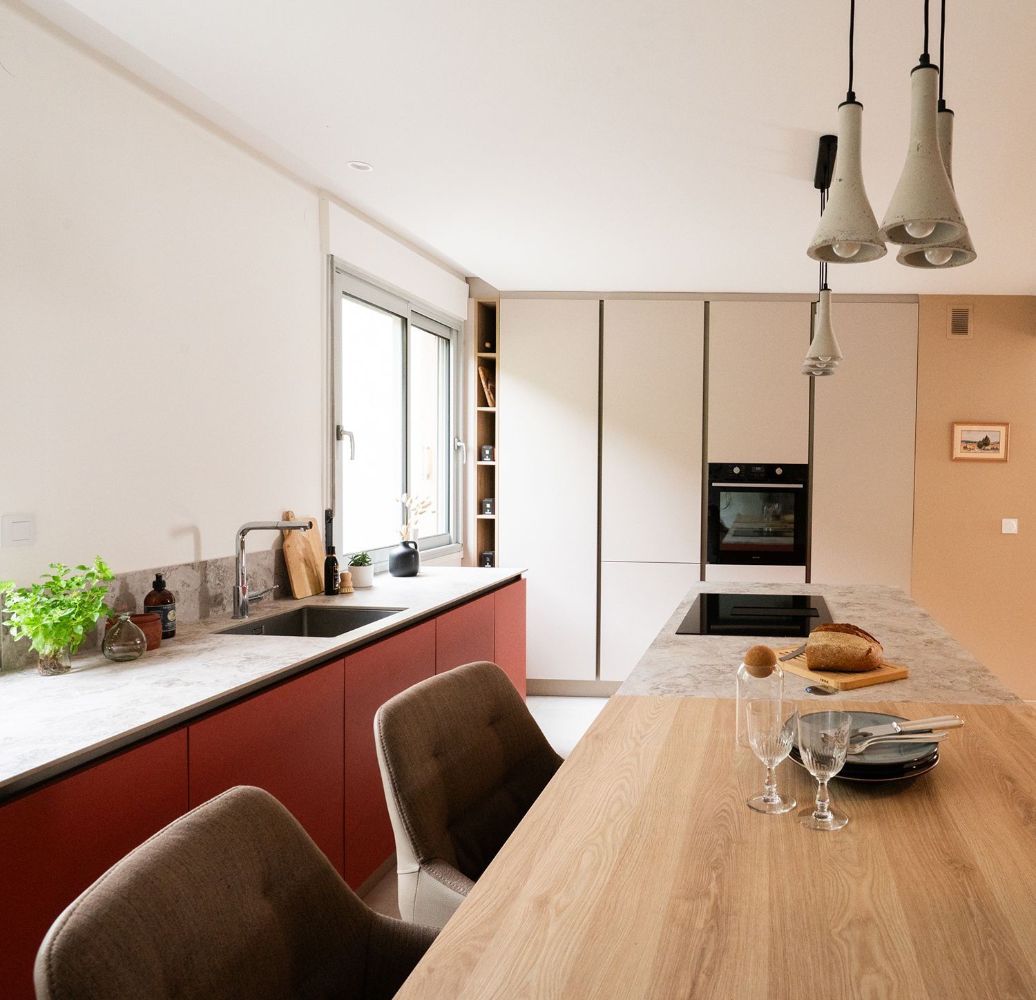 Cuisine moderne avec placards rouges, îlot en bois et appareils électroménagers aux couleurs neutres.