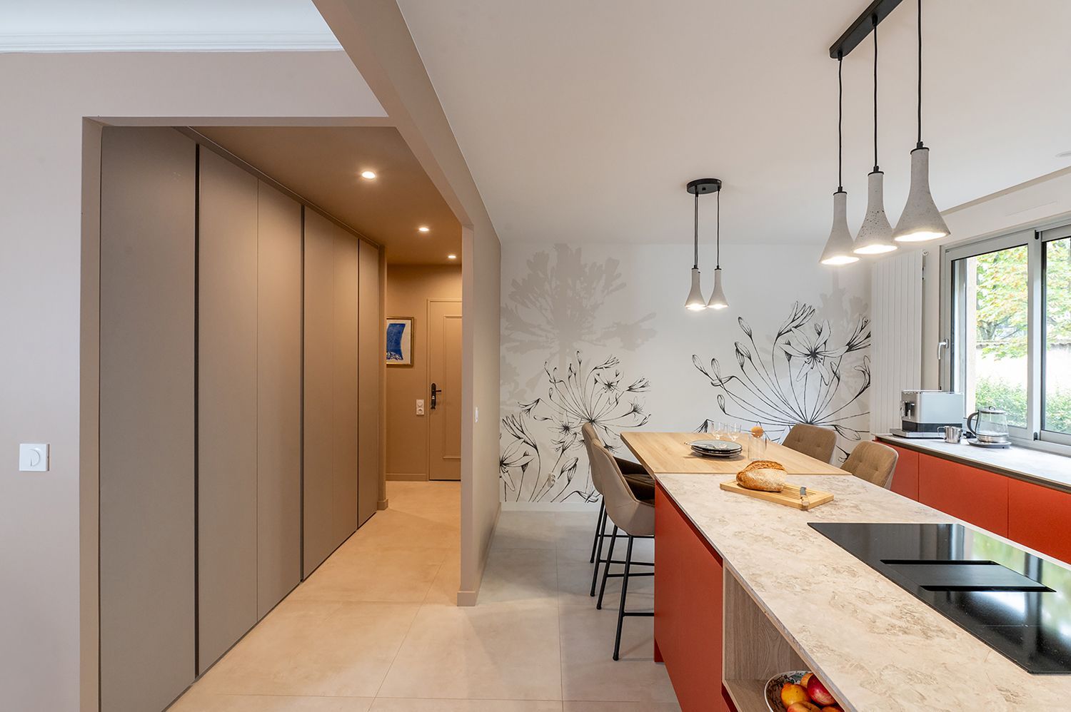 Cuisine moderne avec îlot rouge, suspensions lumineuses et placards intégrés.