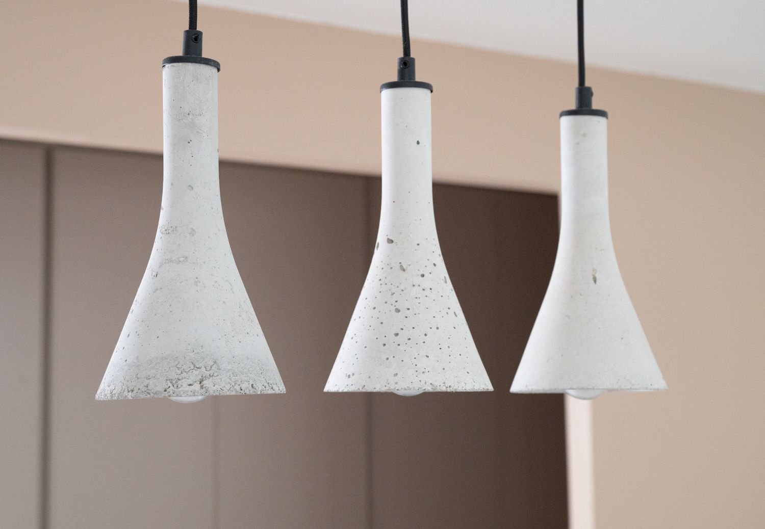 Trois suspensions en béton ornent un plafond, sur un fond beige flou.