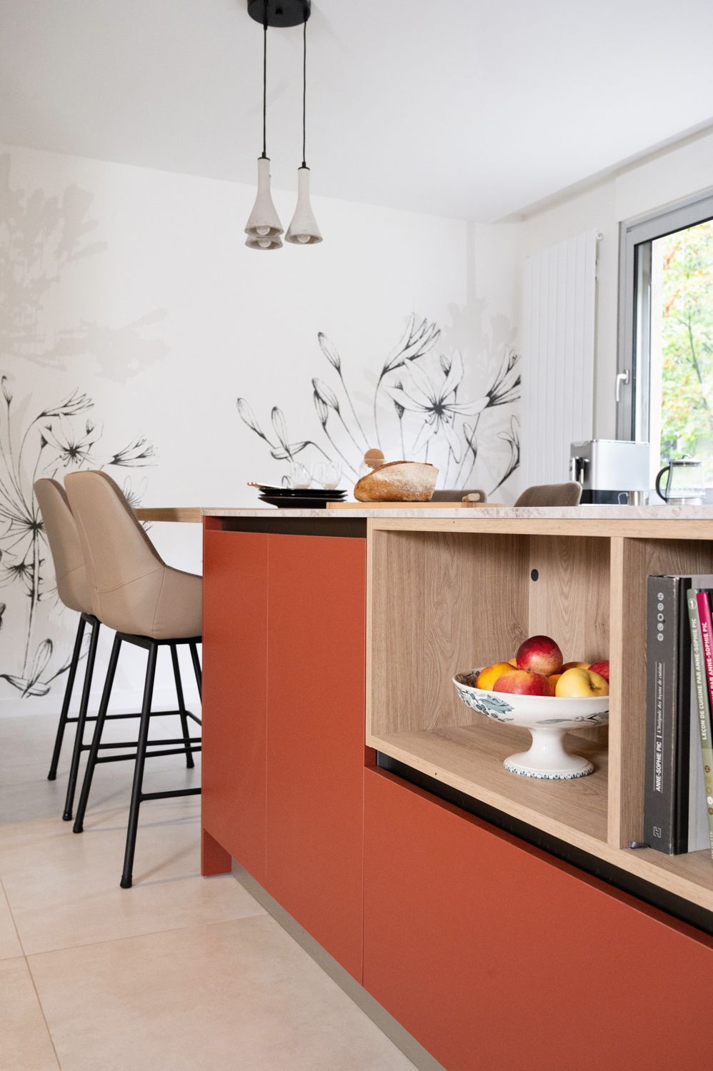 Îlot de cuisine avec placards couleur rouille, plan de travail en bois clair et étagère intégrée. Tabourets de bar beiges.