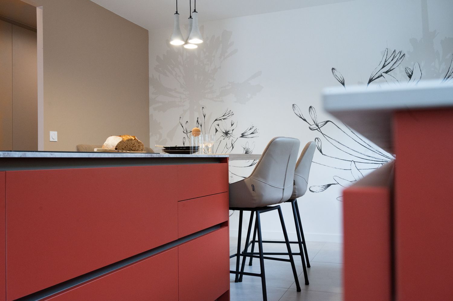 Îlot de cuisine rouge avec deux tabourets de bar, tableau mural floral blanc et mur beige.