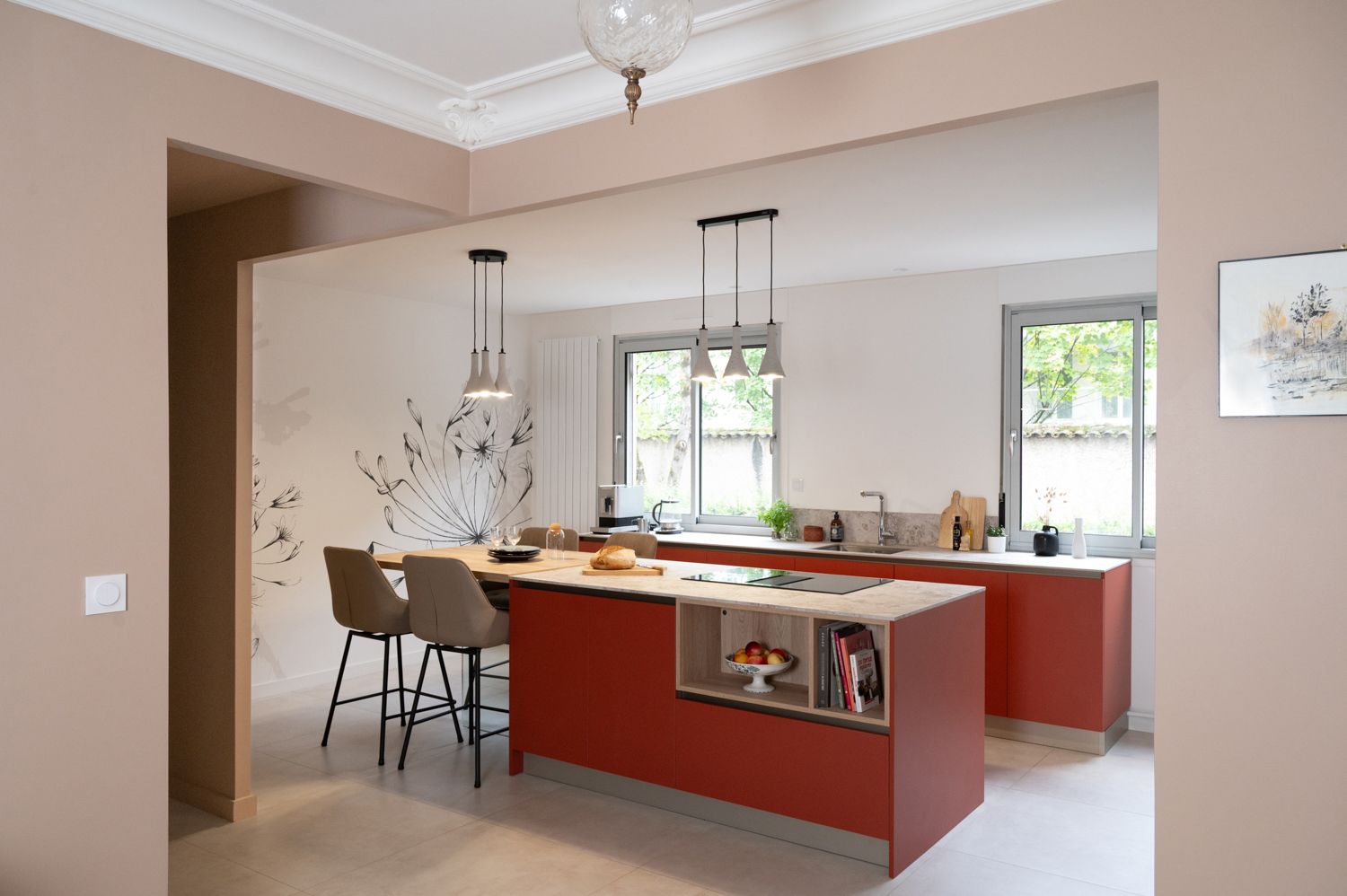 Cuisine rouge moderne avec îlot central et tabourets de bar, décoration murale florale et deux fenêtres.