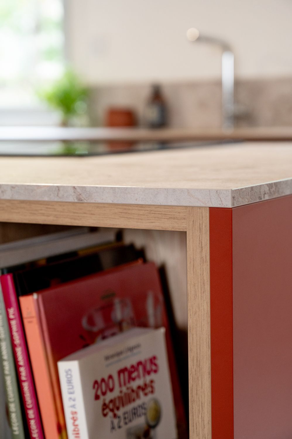 Gros plan sur un îlot de cuisine avec bibliothèque intégrée. L'îlot est rouge avec des finitions en bois. Des livres remplissent les étagères.