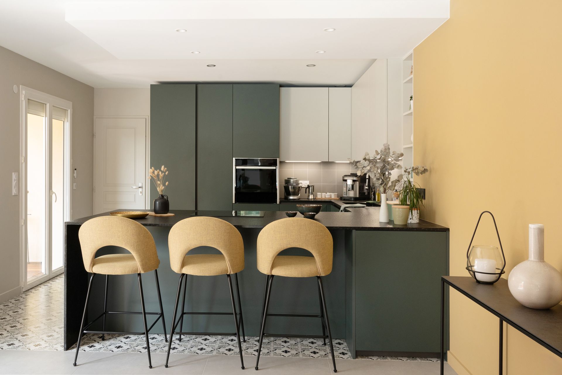 Cuisine moderne avec placards vert foncé, îlot central avec tabourets jaunes et mur d'accent jaune.