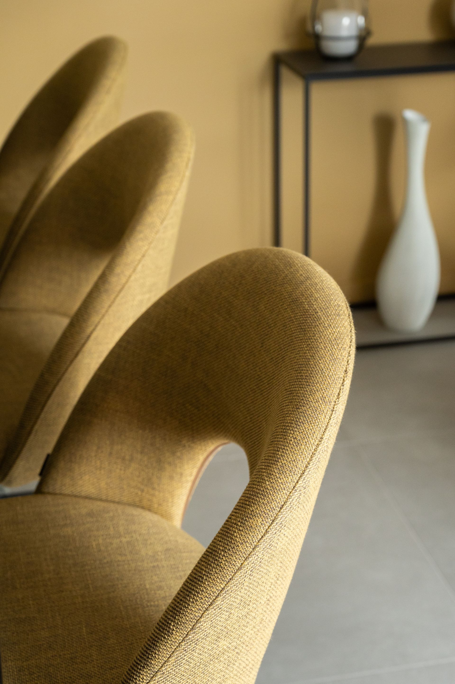 Fauteuils jaunes capitonnés, orientés vers la caméra. Vase et étagère en arrière-plan.