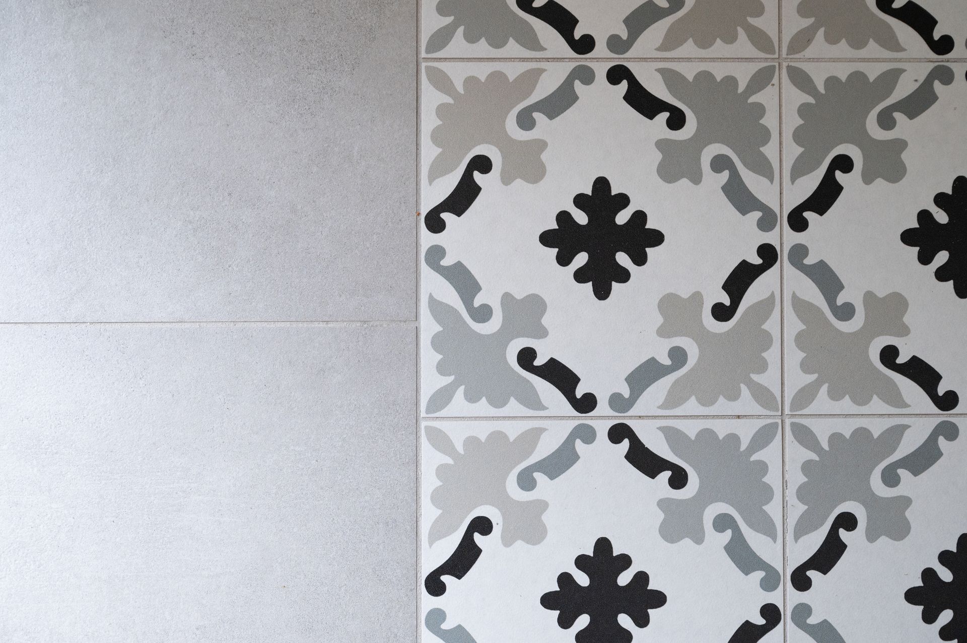 Un carrelage gris et blanc à motifs au sol, jouxtant un mur texturé gris clair.