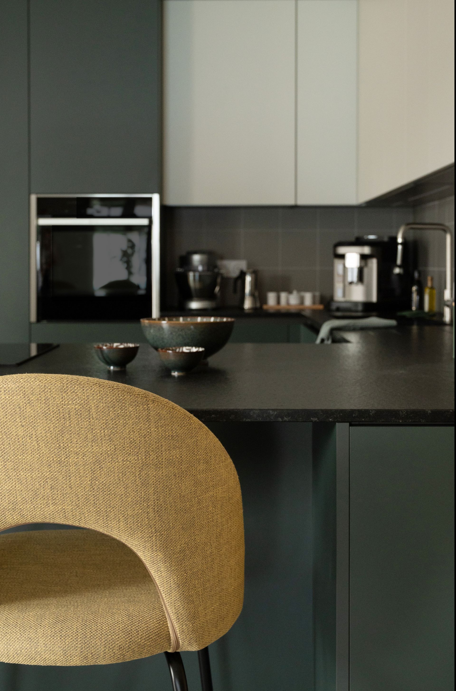 Cuisine avec placards gris foncé, placards hauts blancs et tabouret de bar beige.