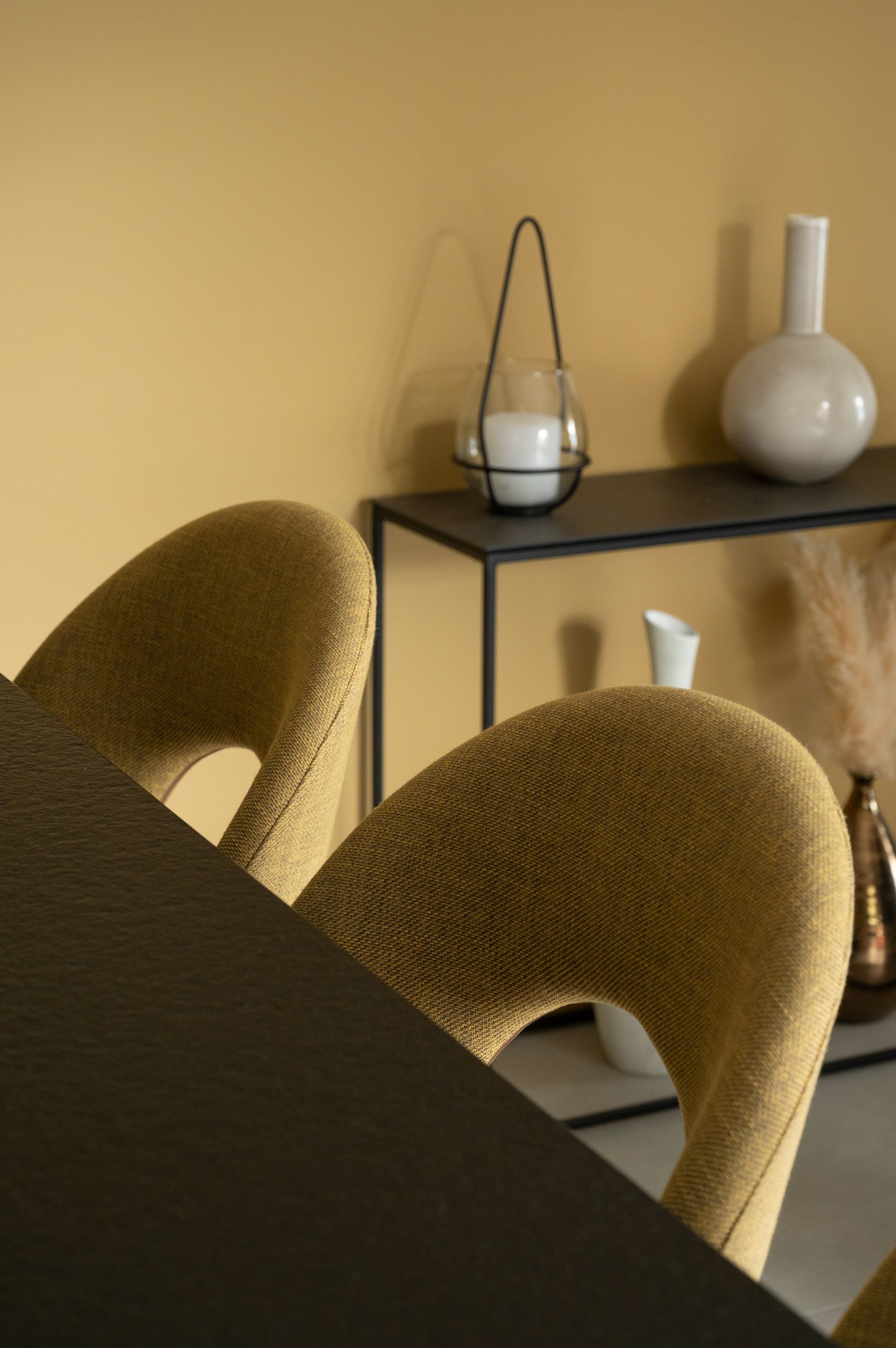 Deux fauteuils jaunes capitonnés et une table noire. Étagère avec vases et bougeoir.