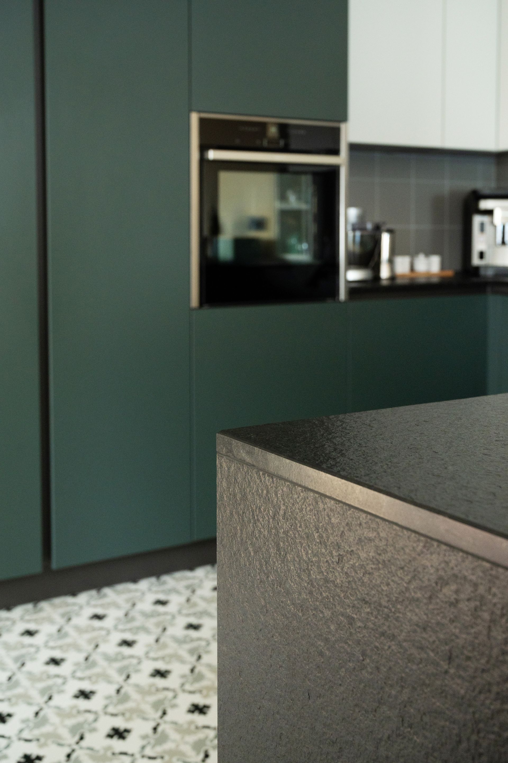 Cuisine moderne vert foncé avec îlot en pierre et sol à motifs.