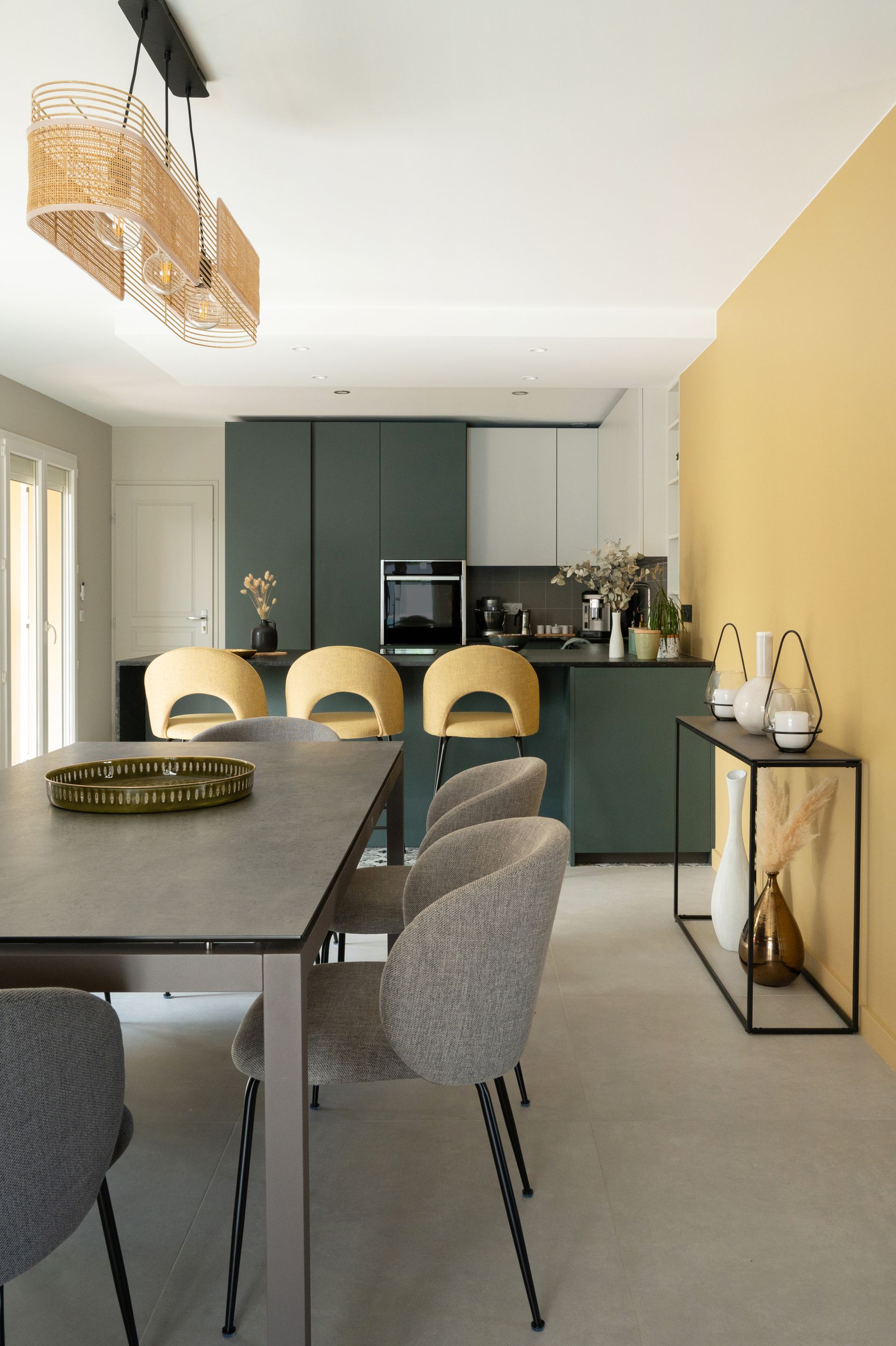 Cuisine et salle à manger modernes avec table grise, placards bleu sarcelle et mur d'accent jaune.