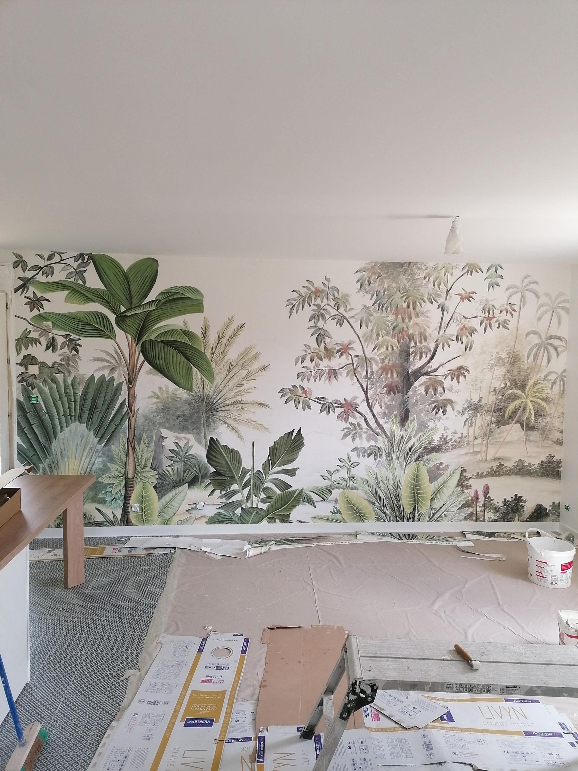 Chambre en cours d'aménagement avec papier peint et sol à motifs jungle. Palmiers, plantes et couleurs neutres.