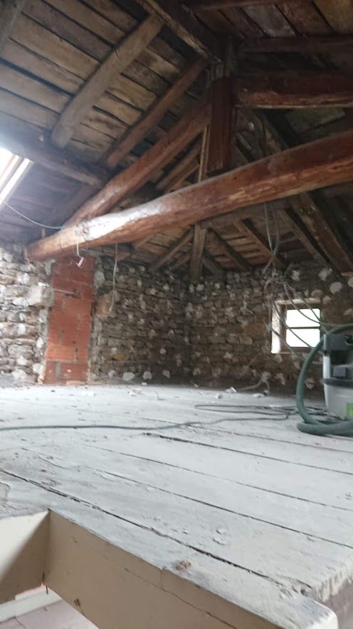 Intérieur d'un grenier rustique avec poutres apparentes, murs en pierre et plancher en bois.