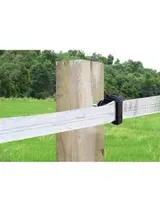 Cinta de cerca eléctrica enrollada alrededor de un poste de madera en un campo de hierba.