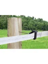Cinta de cerca eléctrica negra sujeta a un poste de madera en un campo verde con árboles al fondo.