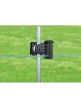 Aislador negro para cerca eléctrica sujeto a un poste de metal en un campo de hierba.