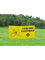 Señal de advertencia amarilla con la inscripción “CERRADO ELÉCTRICO” en un campo verde con árboles detrás.