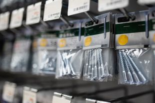 Pasillo de ferretería con filas de bolsas de tornillos y sujetadores colgando en estantes metálicos.