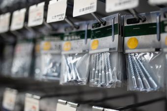 Pasillo de ferretería con filas de bolsas de tornillos y sujetadores colgando en estantes metálicos.