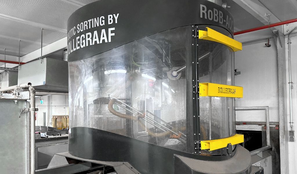 Roboter zur Müllsortierung von Allegraaf. Dunkelgraue und durchsichtige Schutzhülle, gelbe Zierleiste, in einer Fabrikumgebung.