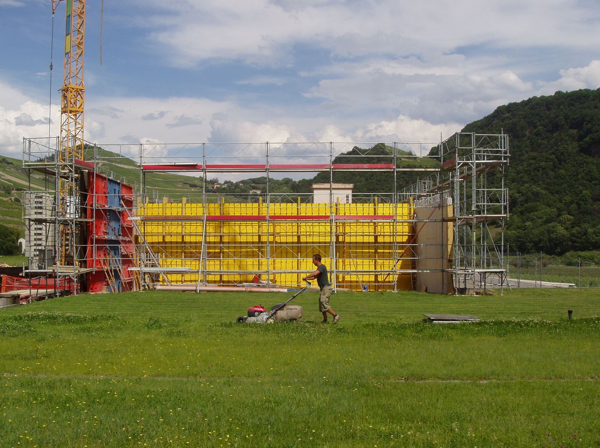 Un homme tond la pelouse devant un bâtiment en construction