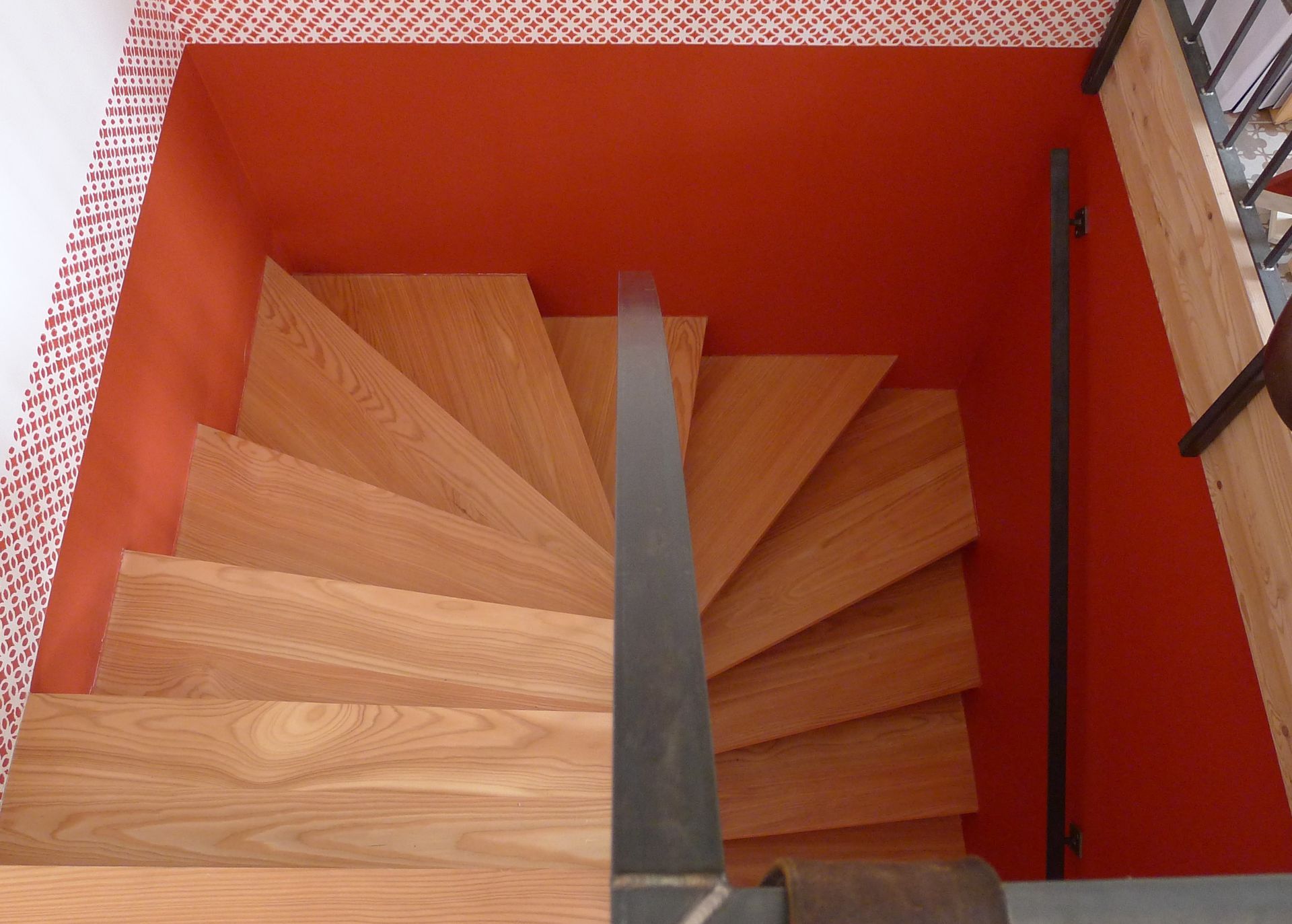 Un escalier en colimaçon en bois avec un mur rouge derrière
