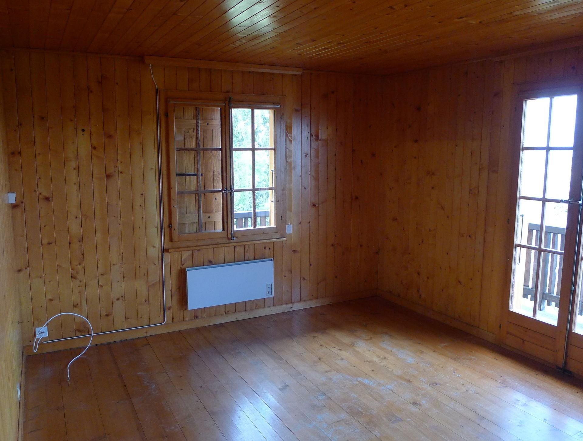 Une pièce vide en bois avec un radiateur et deux fenêtres.