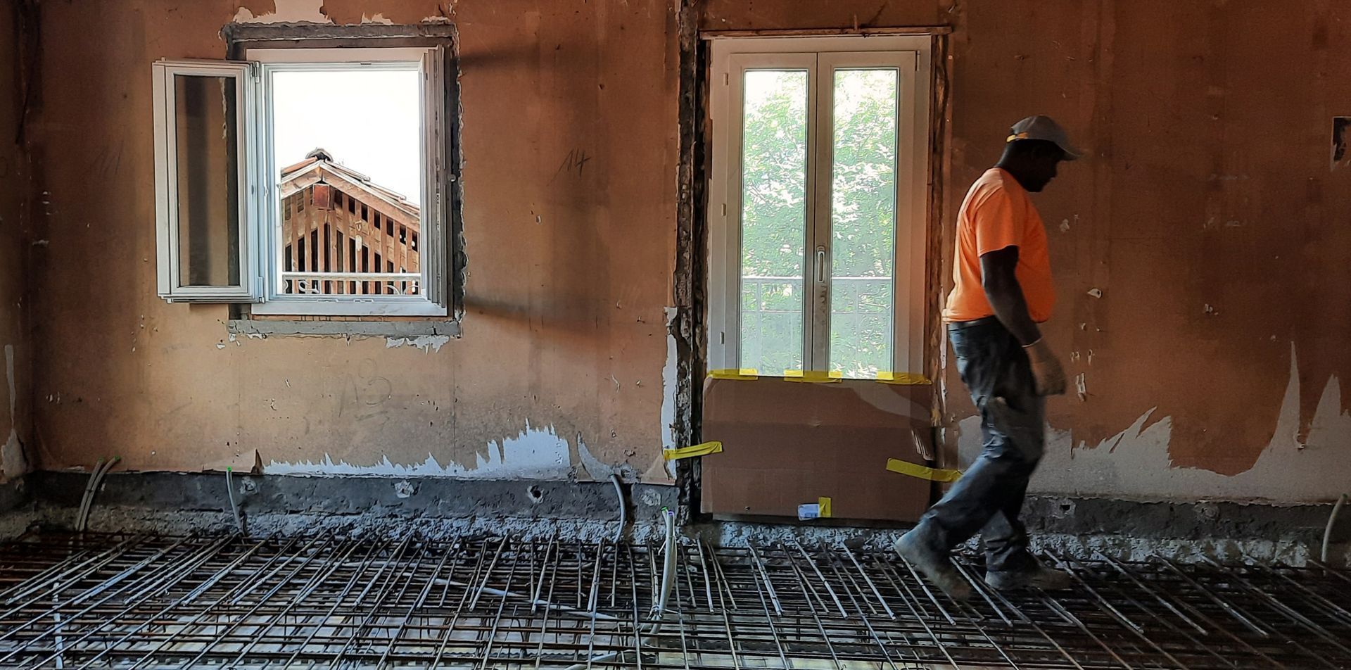 Un homme en chemise orange marche dans une pièce avec une fenêtre