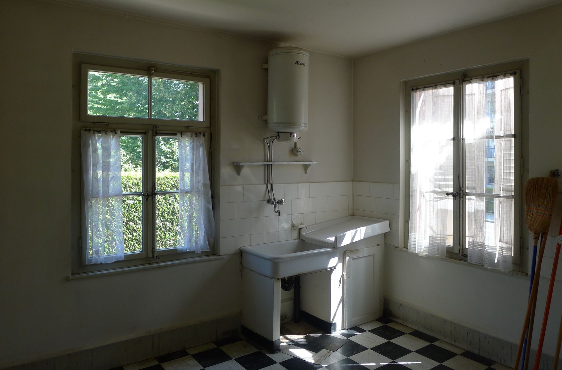 Une cuisine avec un évier et deux fenêtres et un sol en damier.