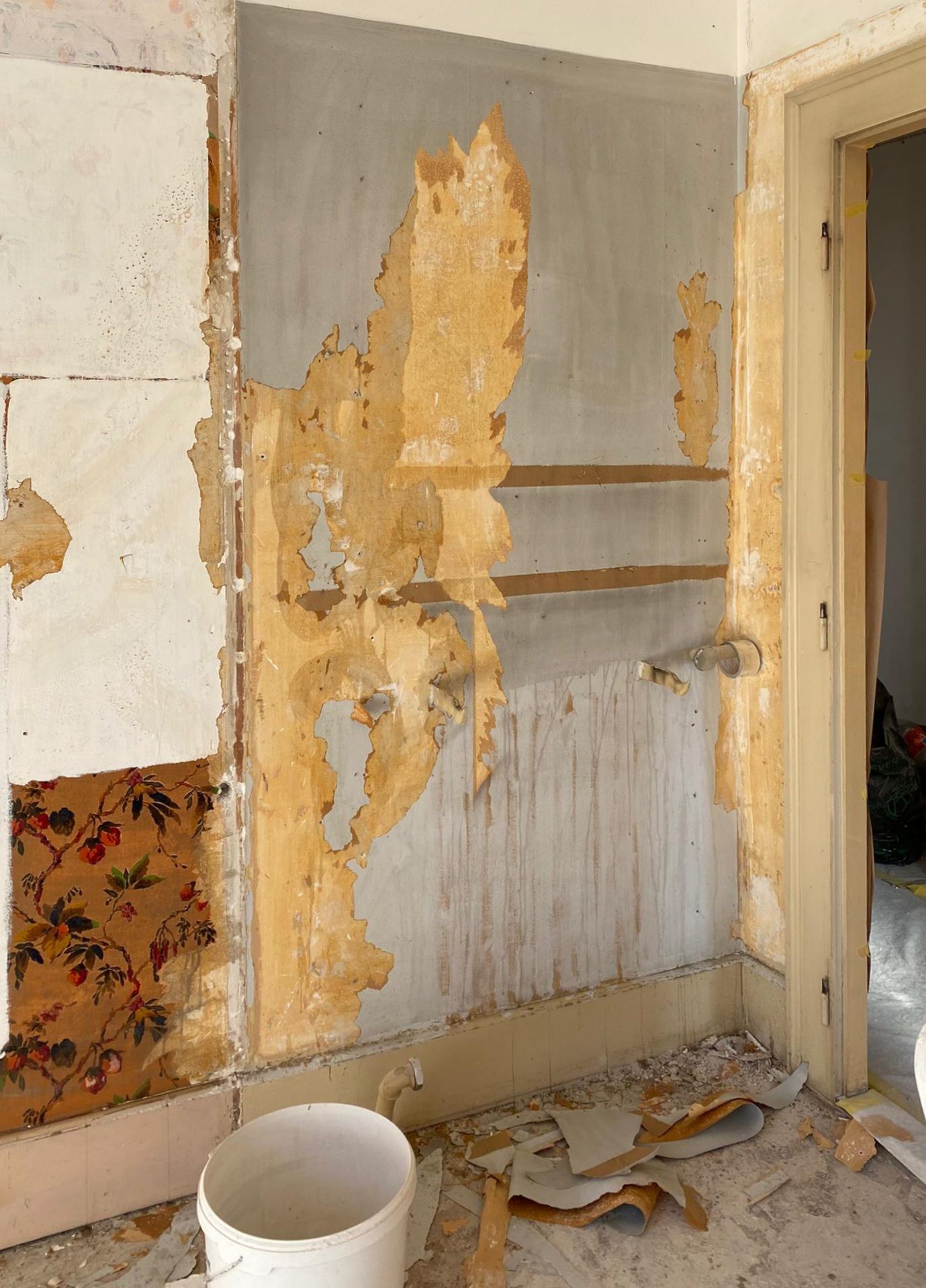 Une pièce avec du papier peint qui pèle et un seau sur le sol
