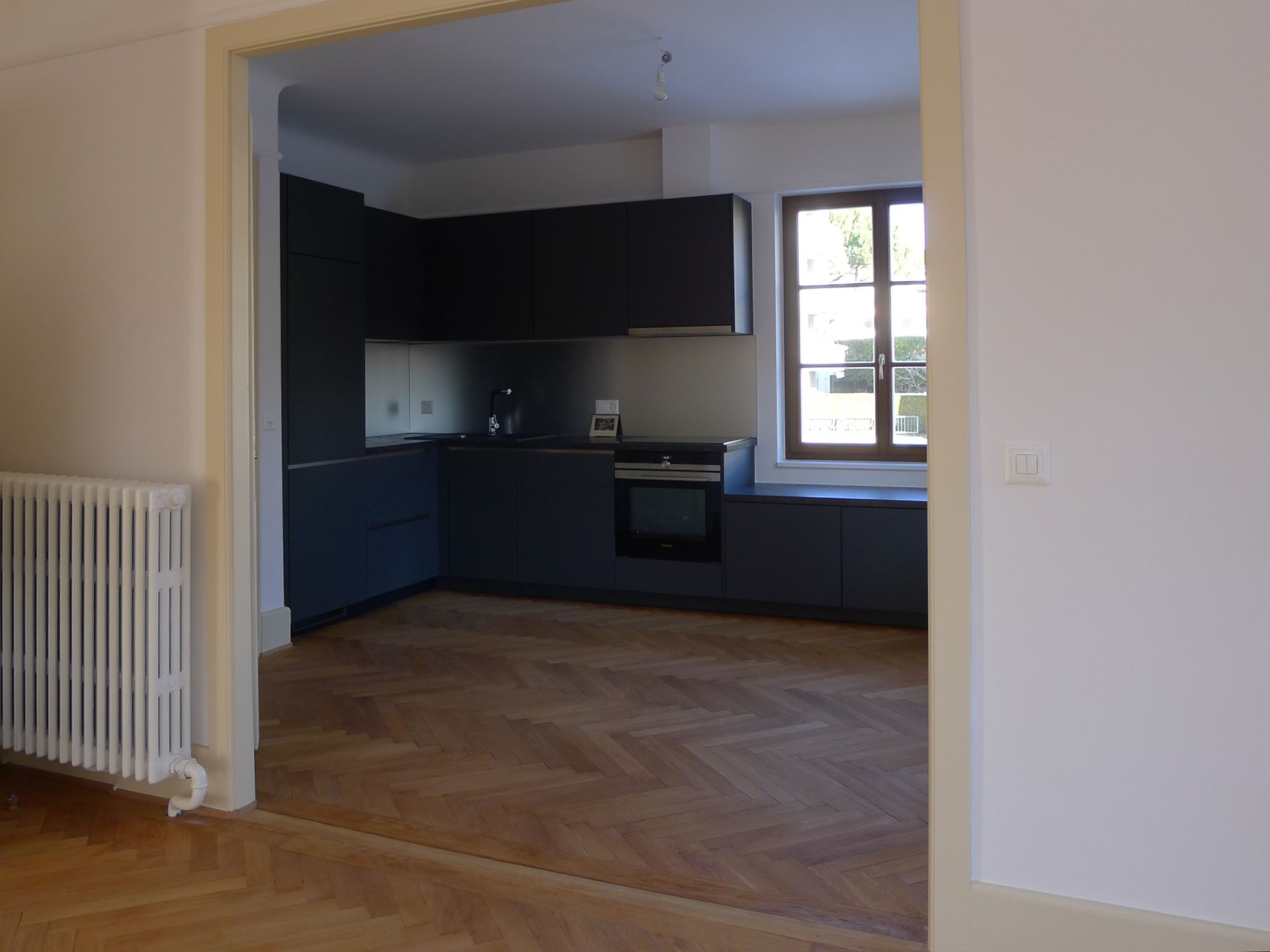 Une cuisine vide avec des armoires noires et un plancher en bois