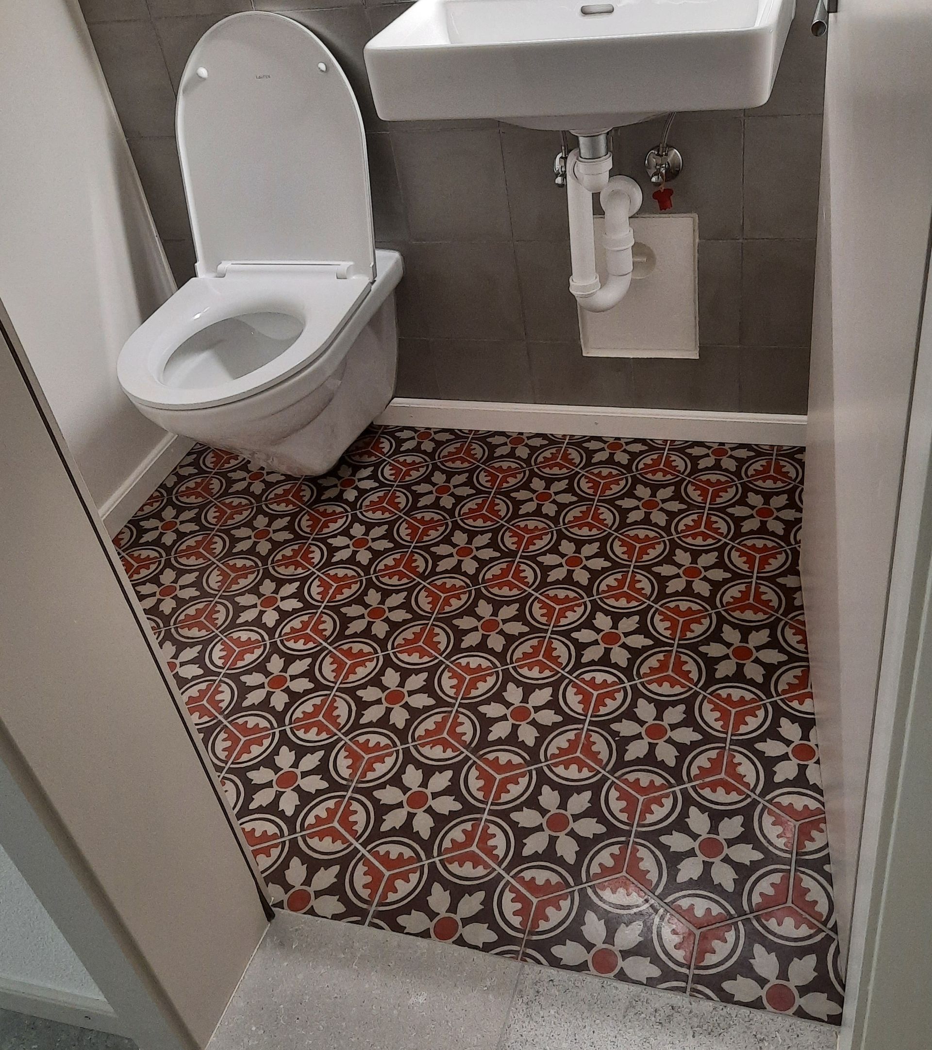 Une salle de bain avec des toilettes, un lavabo et un sol à motifs