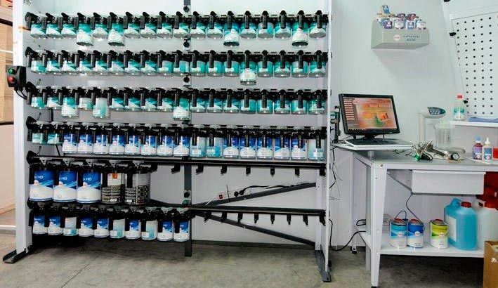 Un estante lleno de botellas de pintura y una computadora en un escritorio.