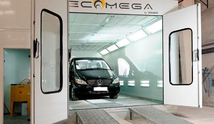 Un coche negro está estacionado dentro de una cabina de pintura.