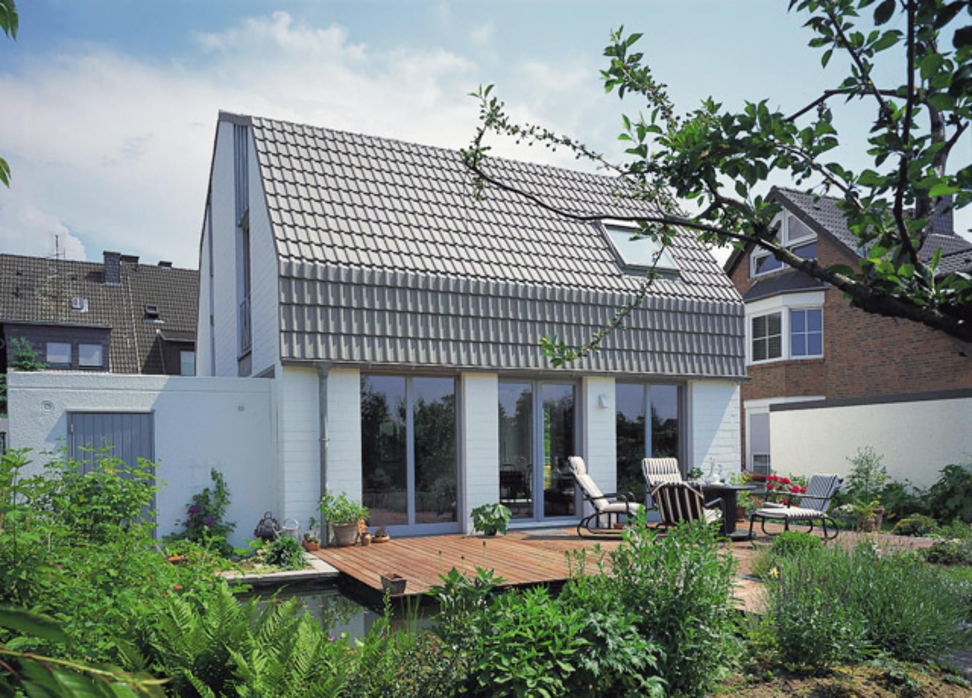 Ein weißes Haus mit grauem Dach steht neben einem Backsteinhaus.
