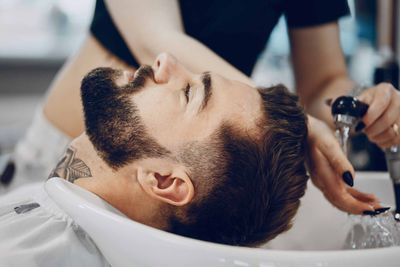 Un homme allongé au lavabo d'un salon de coiffure pendant qu'un coiffeur lui lave les cheveux.