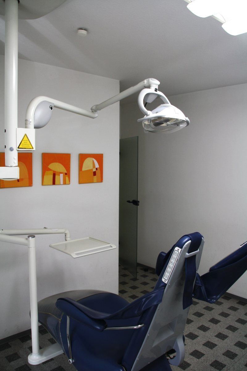 Zahnarztstuhl und Deckenleuchte in einer Zahnarztpraxis. Orangefarbenes Kunstwerk an der Wand.