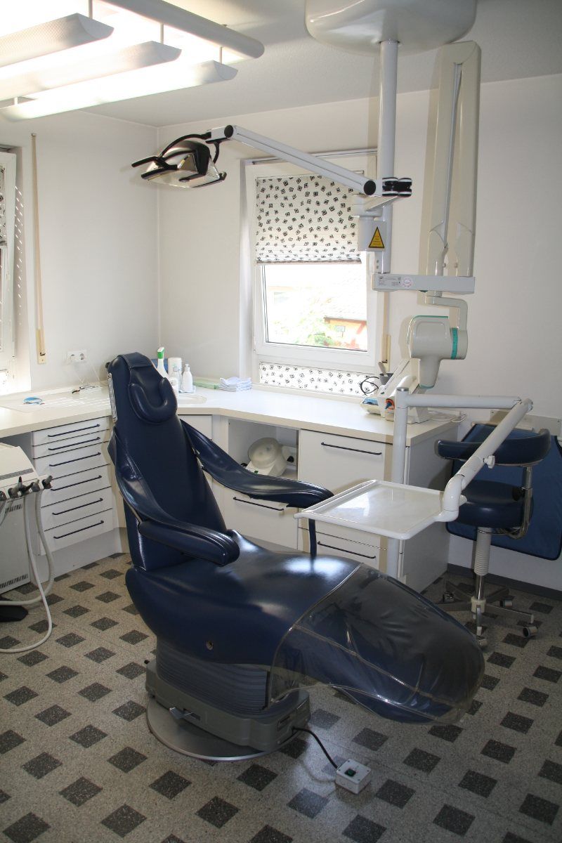 Zahnarztpraxis mit blauem Stuhl und Deckenleuchte.