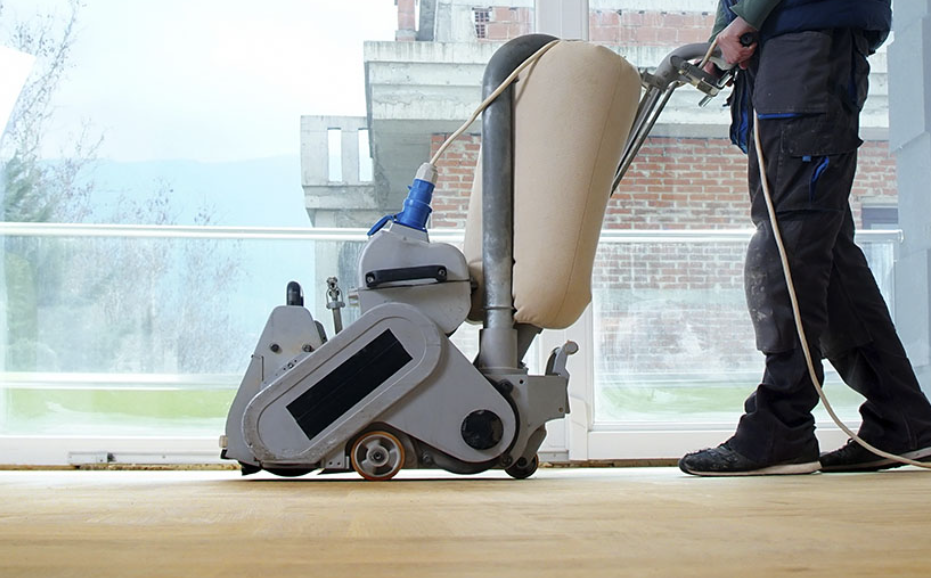 Un hombre está lijando un piso de madera con una máquina.