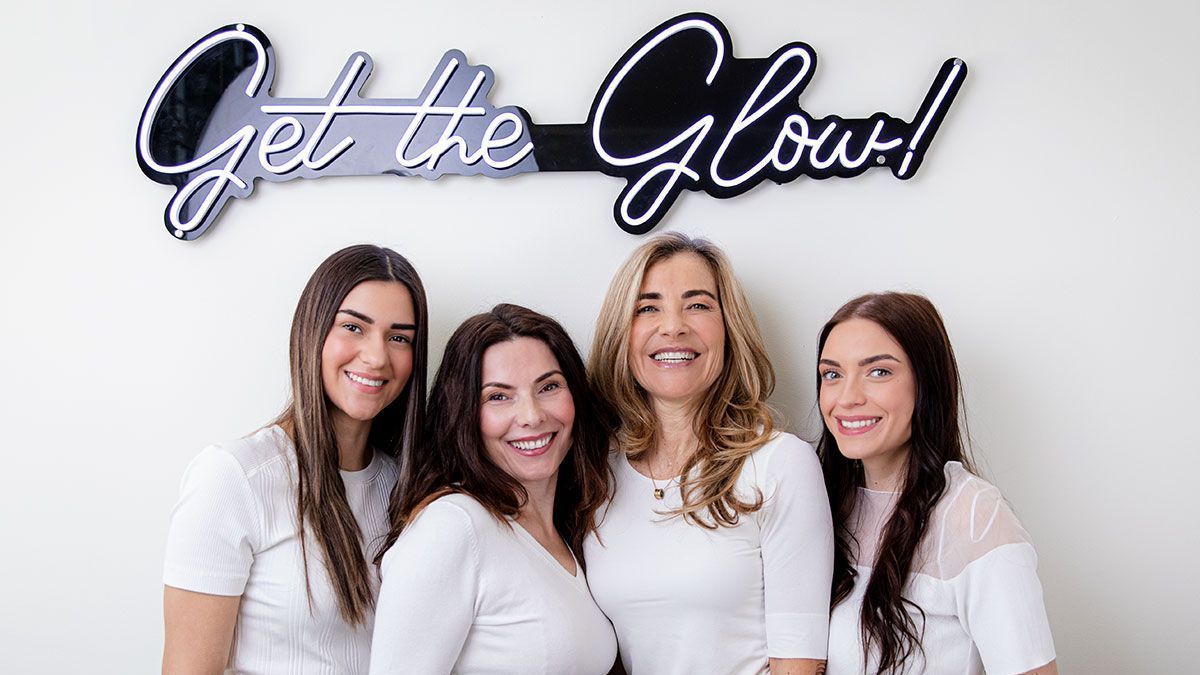 Eine Gruppe von Frauen posiert für ein Foto vor einem Schild mit der Aufschrift „Get the Glow“.