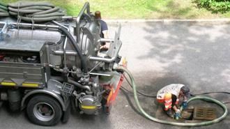 Ein Mann arbeitet neben einem Saugwagen an einem Kanaldeckel.