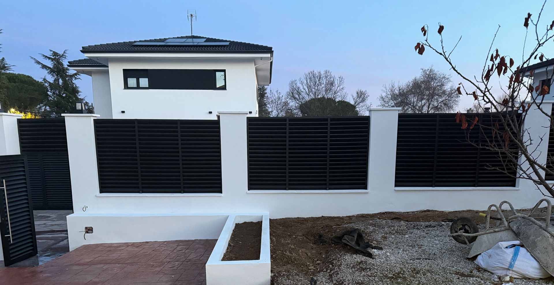 Casa blanca con valla de listones negros al frente, vista desde abajo. Cielo gris.