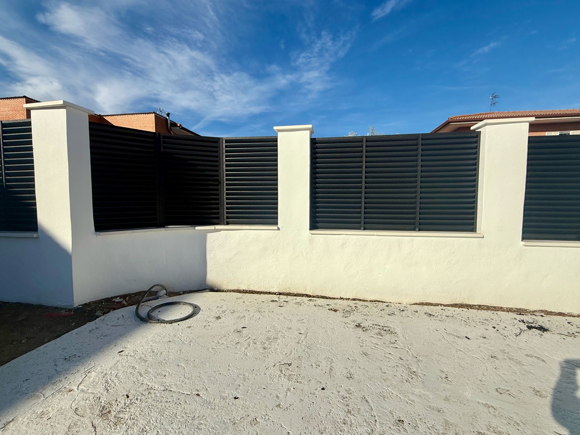 Valla de listones horizontales negros con postes y base blancos contra un cielo azul.