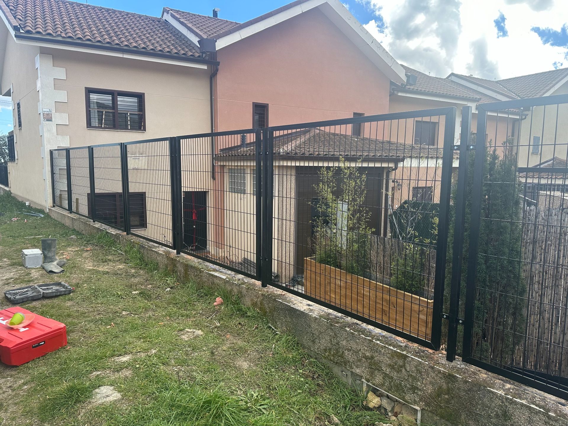 Valla de metal negro a lo largo del patio de un edificio, con césped en primer plano.