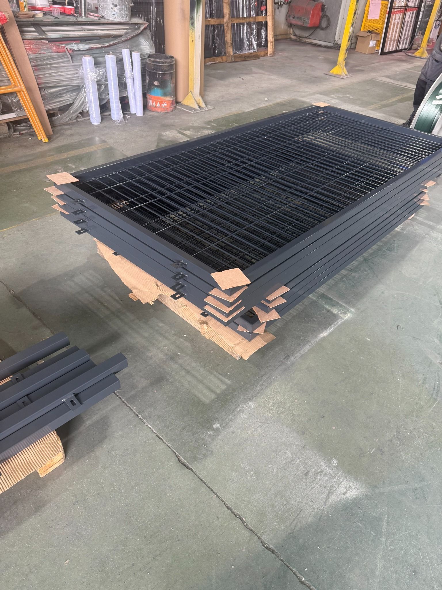 Paneles de valla de metal negro apilados en el suelo de una fábrica.