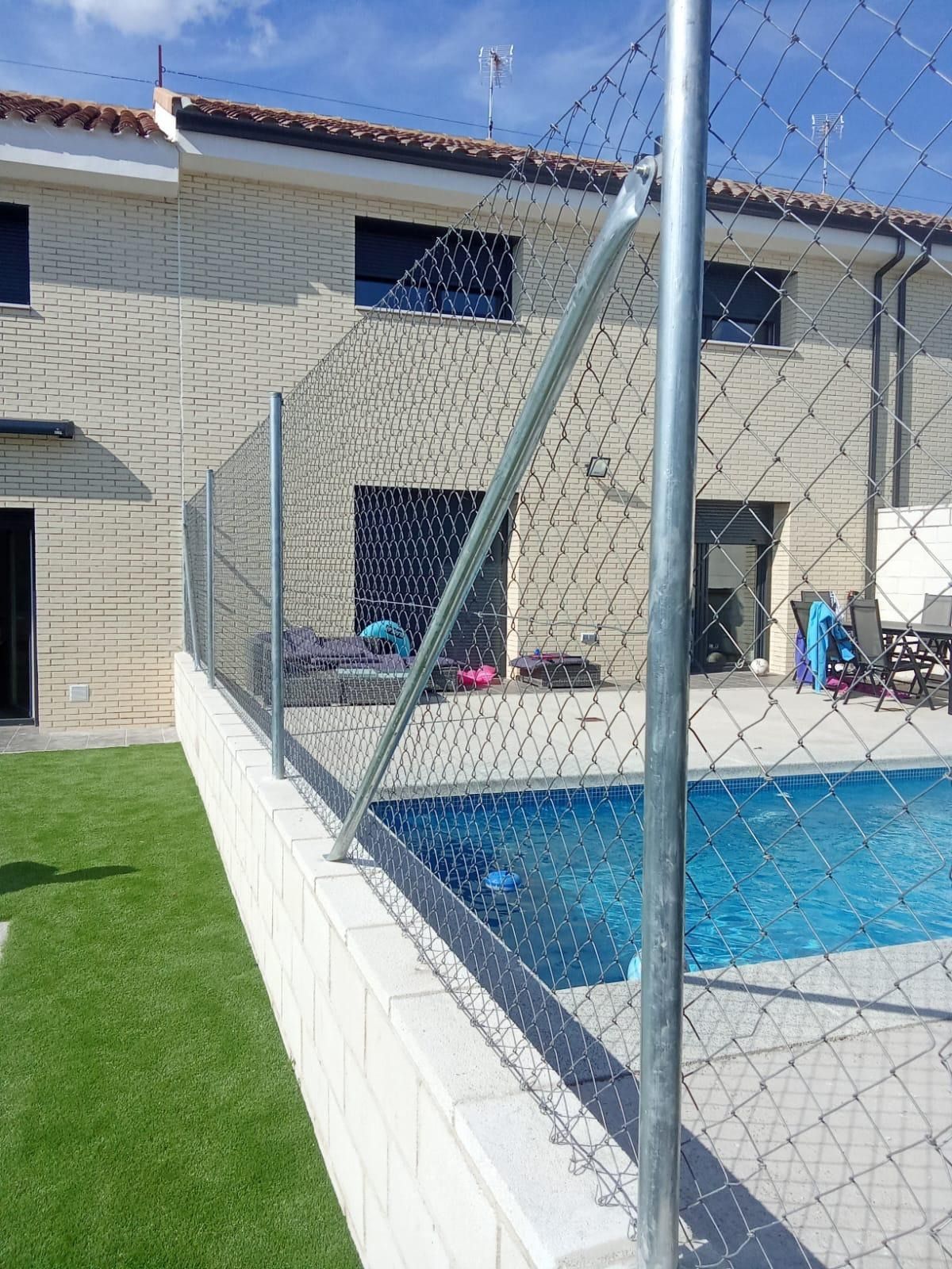 Piscina con valla de seguridad junto a una casa de dos plantas, en un día soleado.