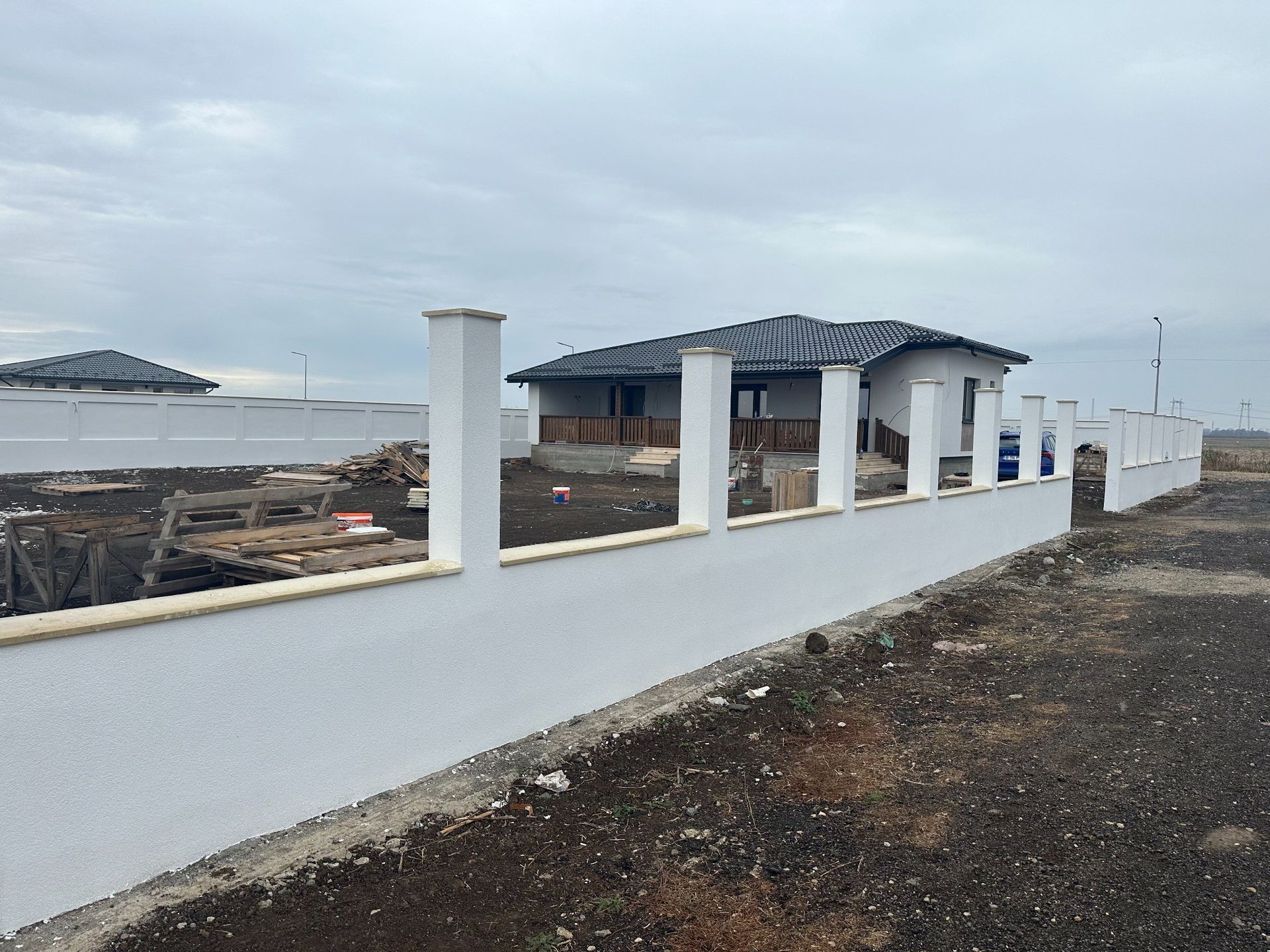 Una valla blanca con postes decorativos rodea una pequeña casa bajo un cielo nublado.