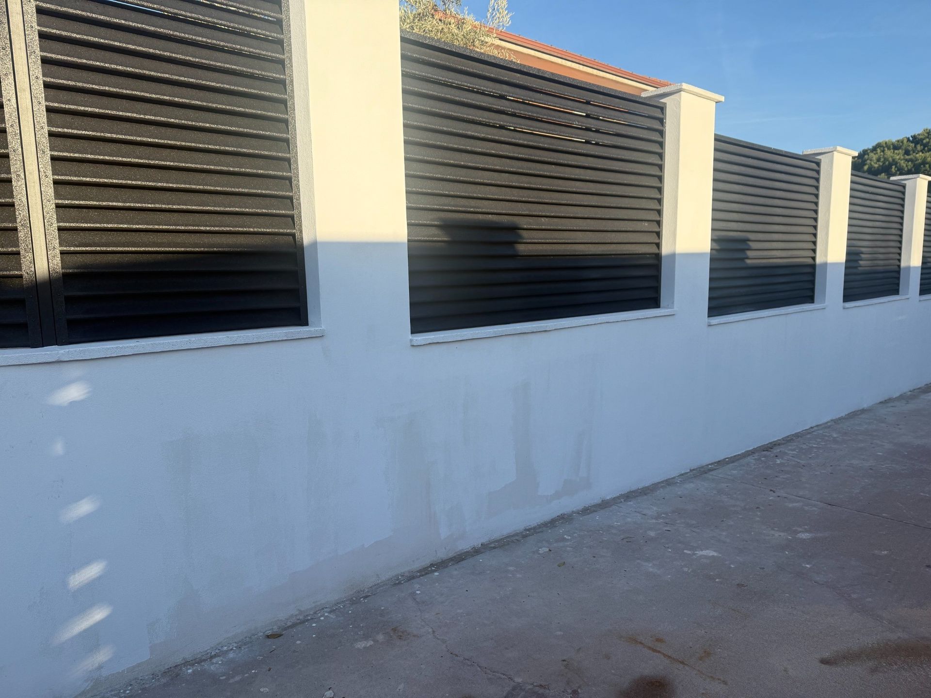 Muro blanco rematado con valla de listones negros y pilares blancos.